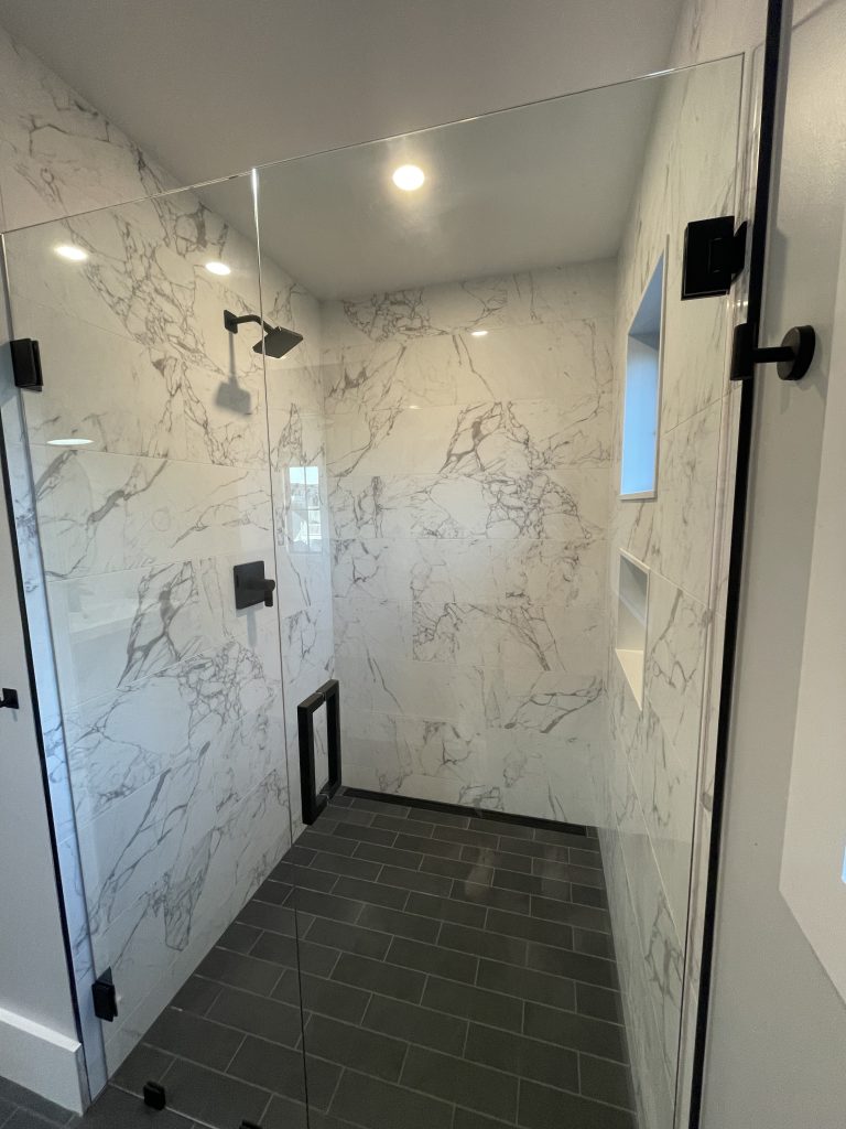 Walk-in shower with marble-look tile and a frameless glass door