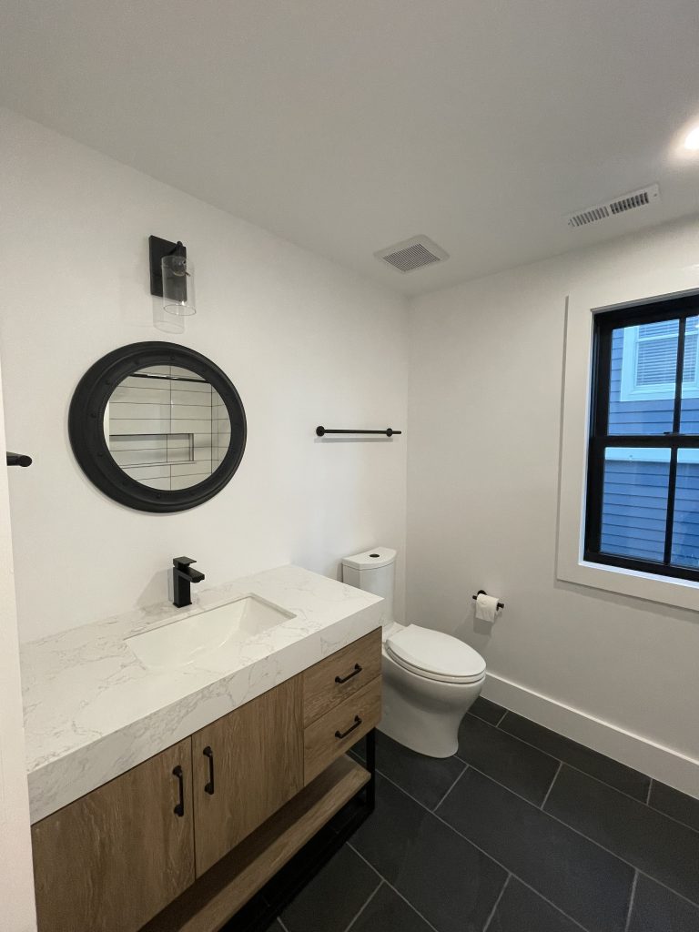 Bathroom with a floating wood vanity, round mirror and dark tile floor